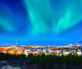 Northern lights illuminate the sky above Reykjavik's city center, showcasing vibrant colors against a dark backdrop.