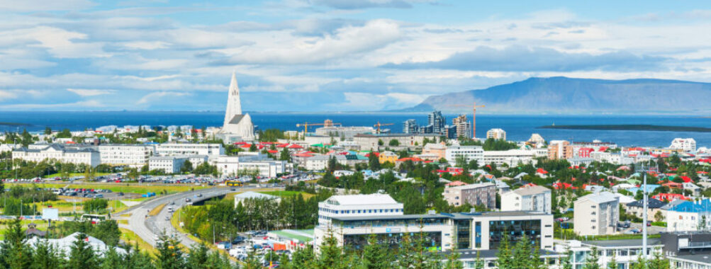 Panoramic view of Reykjavik, Iceland, showcasing colorful buildings and the surrounding mountains under a clear blue sky.