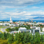 Panoramic view of Reykjavik, Iceland, showcasing colorful buildings and the surrounding mountains under a clear blue sky.