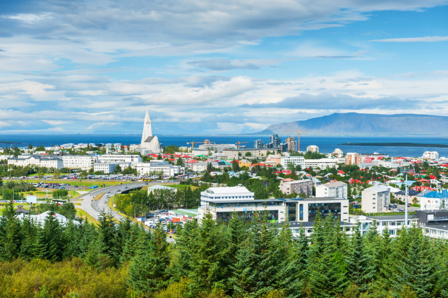 Panoramic view of Reykjavik, Iceland, showcasing colorful buildings and the surrounding mountains under a clear blue sky.