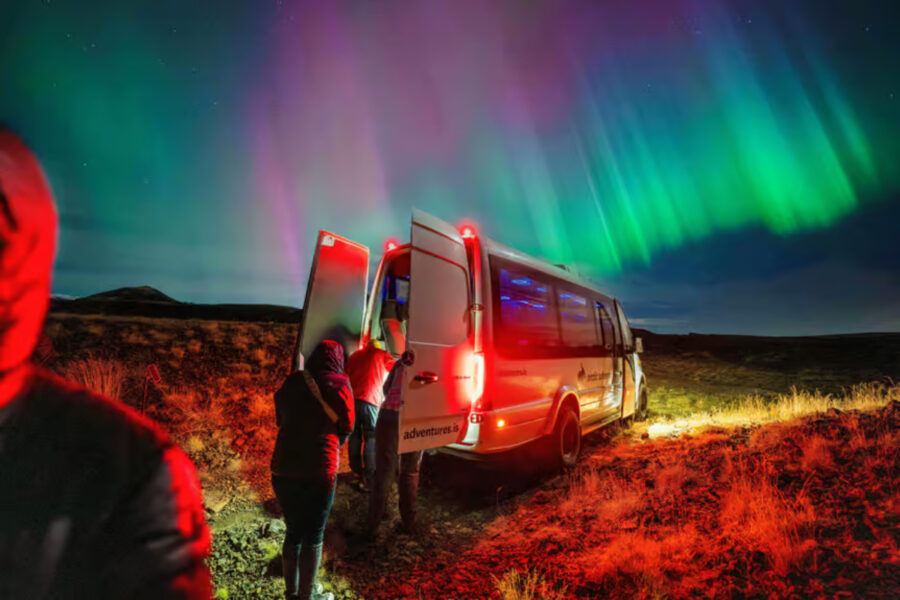 People stand near a van under vibrant aurora borealis lights during the Reykjavík Northern Lights Minibus Tour.
