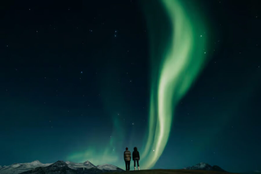 Two people stand beneath vibrant aurora borealis lights in the sky during a Reykjavík Northern Lights Tour.