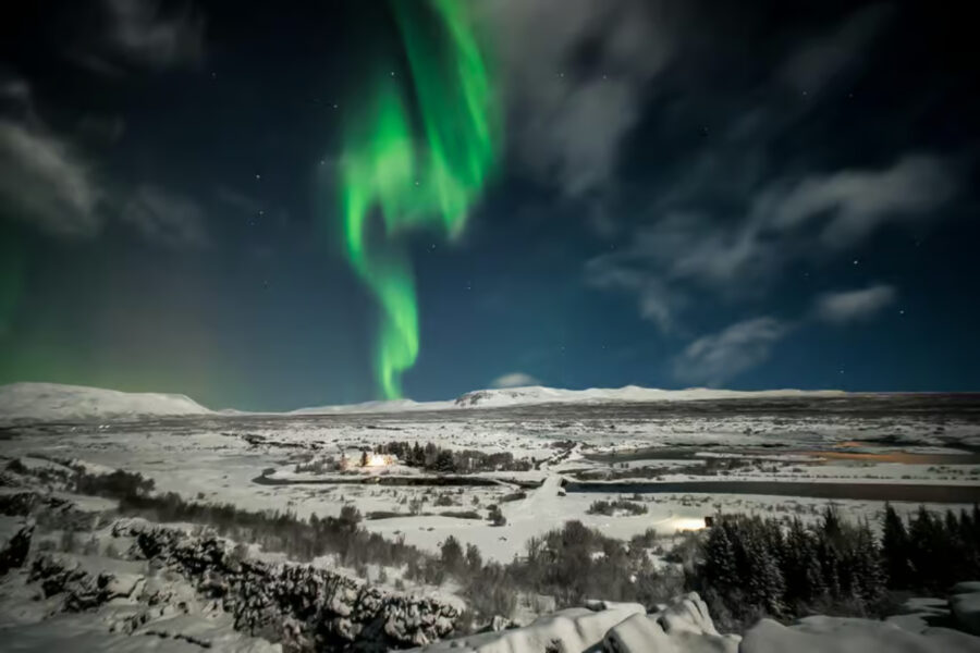 The aurora borealis illuminates the night sky above a snowy landscape during a Reykjavik Northern Lights tour.