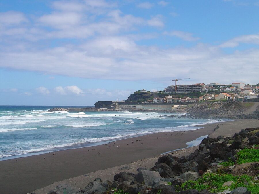Scenic view of a rocky shore in Ribeira Grande, Portugal, featuring a building far off in the background.
