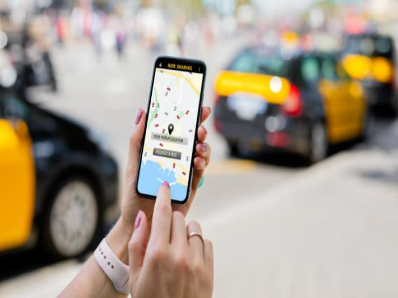 Smartphone showing ride-hailing app map with pickup pin and city taxis on busy street.