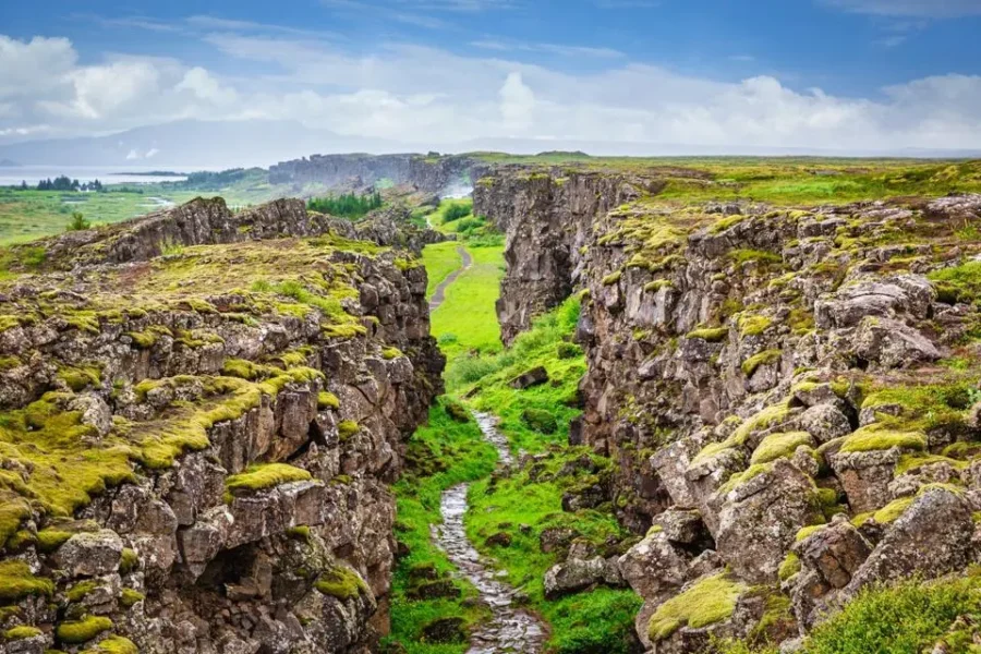 Dramatic canyon with lush greenery and hiking path in Thingvellir National Park landscape.