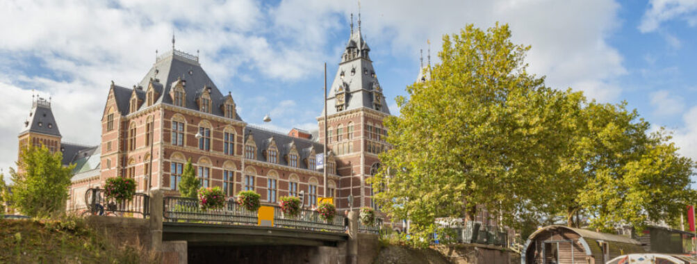 Scenic view of the Rijksmuseum along the canal, highlighting its grand facade and the tranquil waters of Amsterdam.