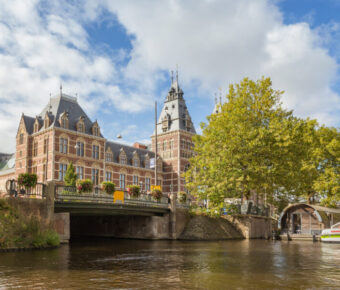 Scenic view of the Rijksmuseum along the canal, highlighting its grand facade and the tranquil waters of Amsterdam.