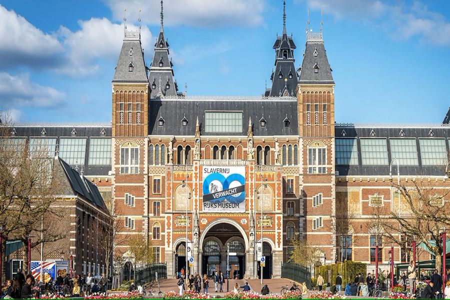 Rijksmuseum facade in Amsterdam showcasing Gothic Revival architecture with bustling visitors in front.