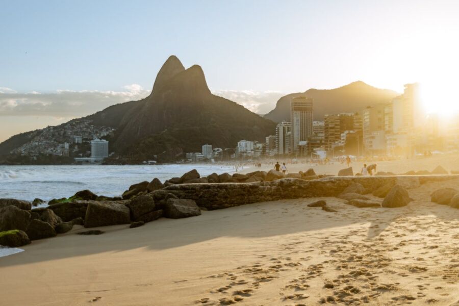 Rio de Janeiro beach at sunset with Dois Irmãos mountains and city skyline.