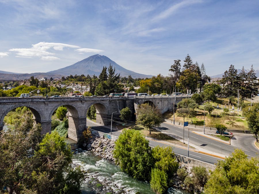 Scenic view of a stone bridge, river, volcano, and park landscape.