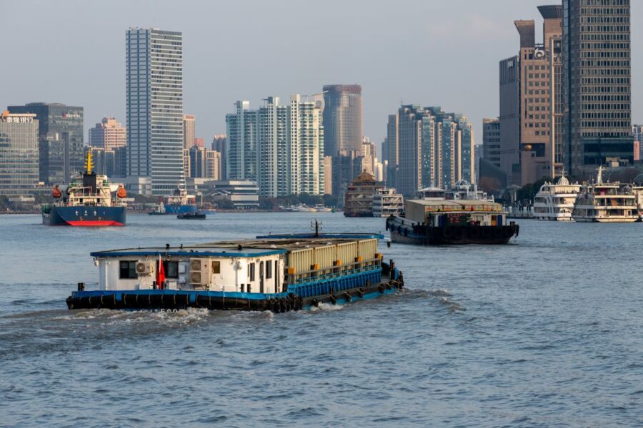 Bustling Huangpu  river cityscape with barge, boats, skyline, and diverse architecture under clear skies.