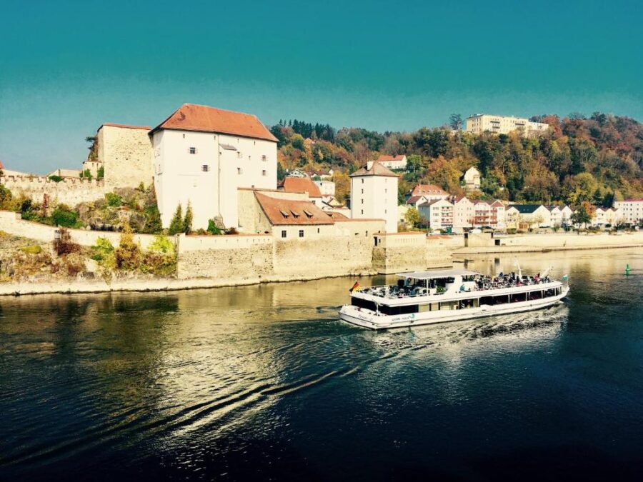 River cruise boat passing historic European riverside fortress and hillside village in autumn.