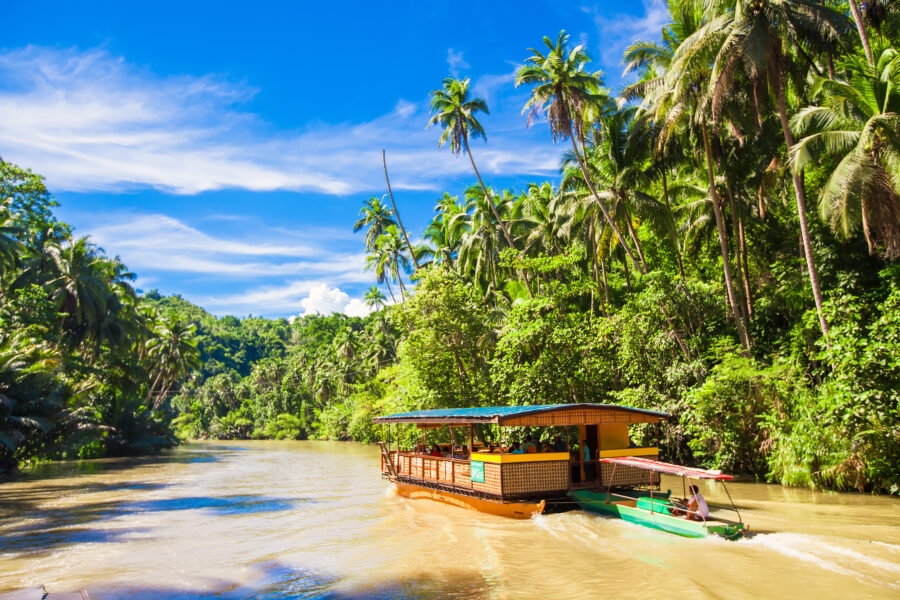 Tourists aboard an exotic cruise boat navigate the lush jungle river in Loboc, Bohol, surrounded by vibrant greenery.
