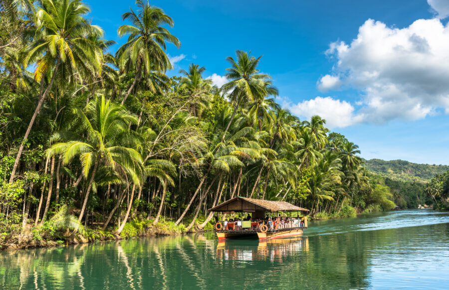 Traditional raft boat with tourists navigating the lush green Loboc River in Bohol, Philippines.