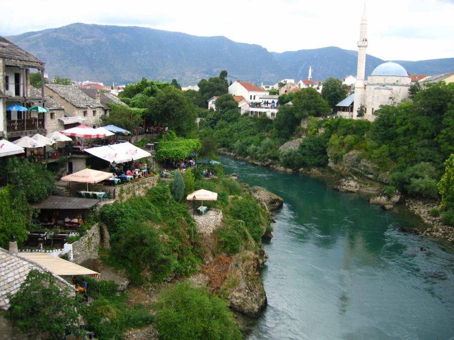 Cityscape of Mostar, Herzegovina, showcasing a clock tower and a bridge spanning the River Neretva.


