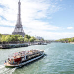 Scenic view of the Eiffel Tower and Seine River, featuring a tourist boat gliding through the picturesque Paris landscape