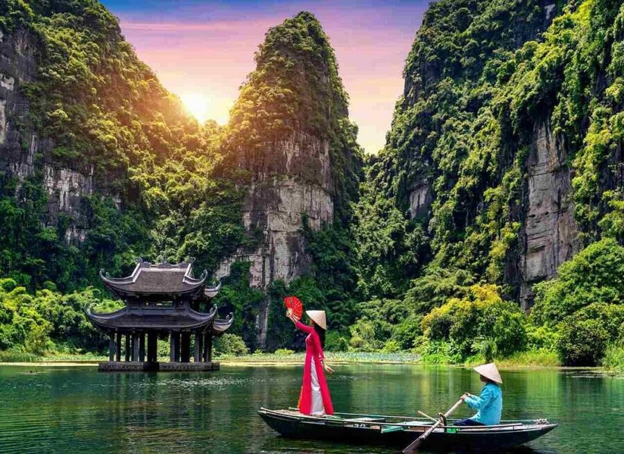 Sunset river valley in Trang An Grottoes with boat, limestone cliffs, pavilion and tourists.
