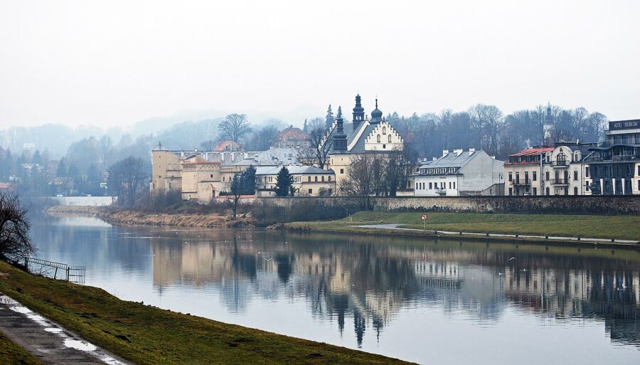 Serene riverside scene featuring historic and modern architecture, misty atmosphere, and tranquil reflections.