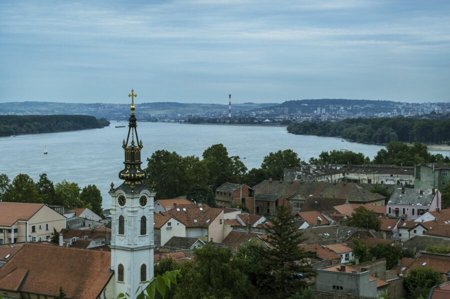 Serene riverside town with church steeple, river, and city skyline in tranquil setting.