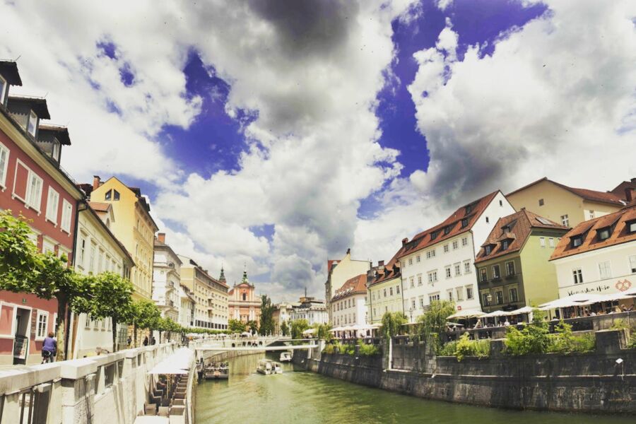 Picturesque riverfront in Ljubljana, Slovenia with charming architecture, lush greenery, and dramatic sky.