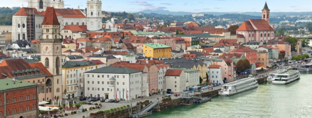 Scenic European riverside town with colorful historic buildings and a grand cathedral under blue sky.