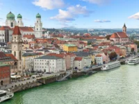 Scenic European riverside town with colorful historic buildings and a grand cathedral under blue sky.