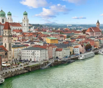 Scenic European riverside town with colorful historic buildings and a grand cathedral under blue sky.
