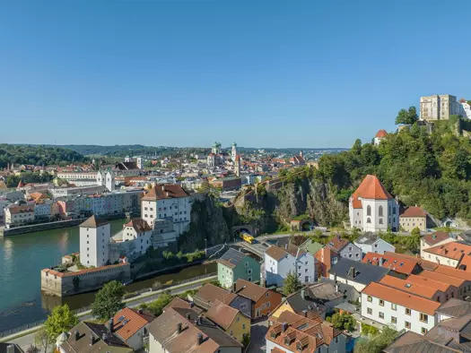 Panoramic view of Grubweg riverside European town with red roofs, church towers, and hilltop fortress.
