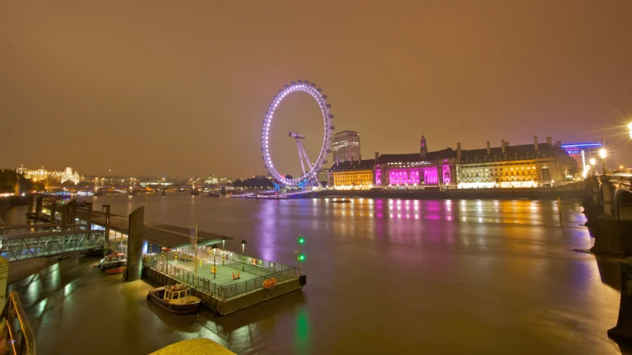 London Eye illuminated Ferris wheel at night reflecting on the River Thames.