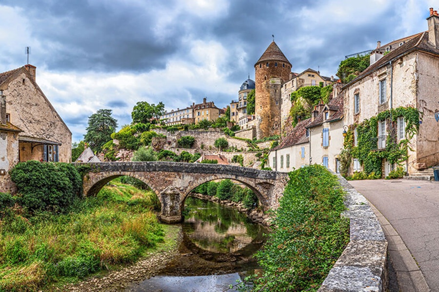 Beaune riverside village with stone arched bridge, river reflections, terracotta roofs and medieval tower.