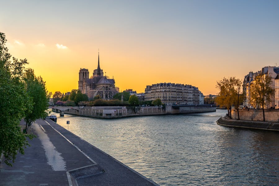 Sunset cathedral on riverside island with promenade, spire reflection and city skyline.