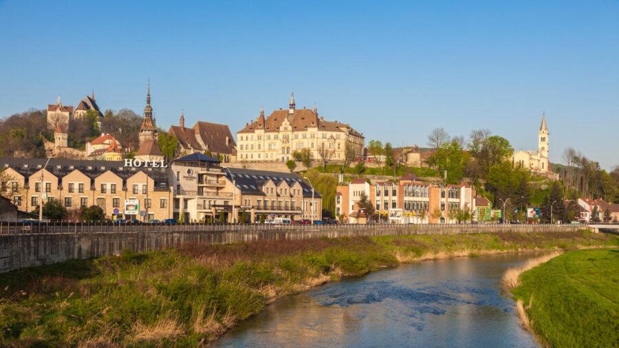 Sighisoara, Romania riverside town with riverfront hotel, historic hillside towers and church spires.