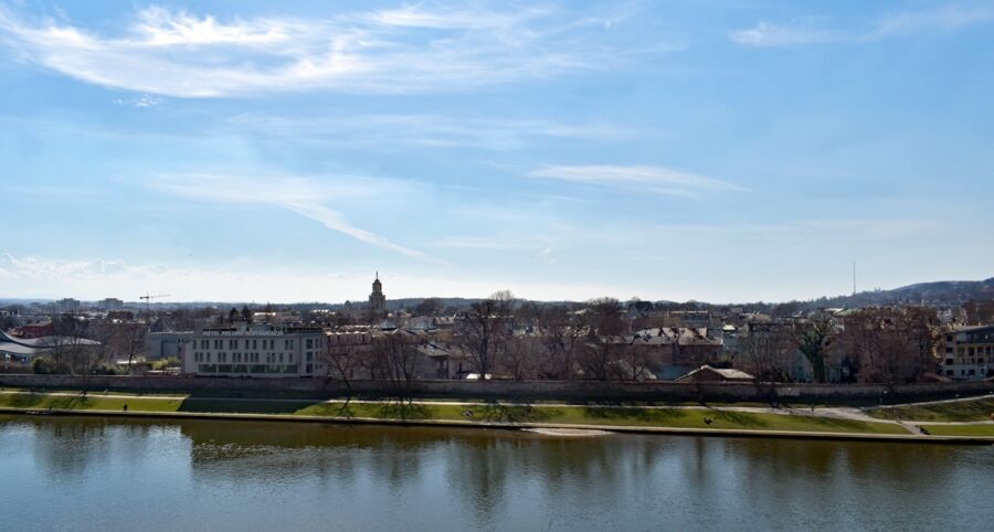 Scenic riverside landscape with urban architecture, nature, clock tower, and recreational activity.