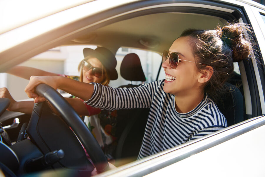 Two young women joyfully driving in a car during a road trip