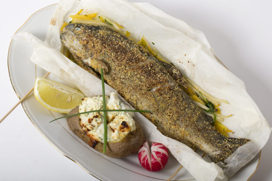 Herb-crusted roasted whole fish with baked potato, lemon wedge on gold-rimmed plate.