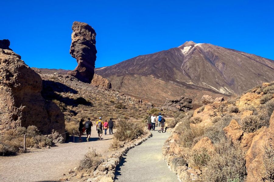 Rock formation with hikers, volcanic mountain, clear sky, and rugged nature landscape.