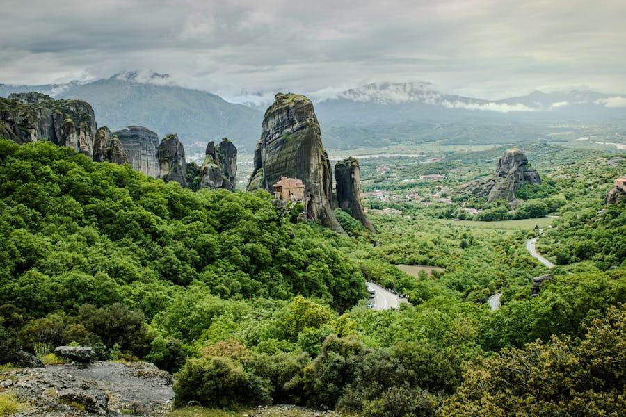 Meteora rock pillars with cliff-top monastery overlooking misty green valley, Greece.