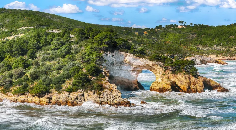 Dramatic coastal arch with lush cliffs, vibrant sea, and serene sky in Gargano National Park.