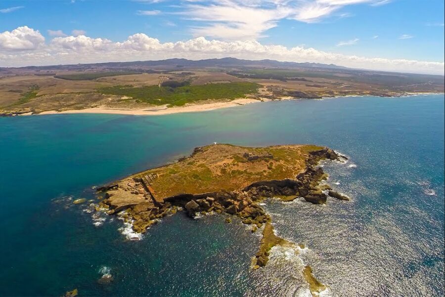 Ilha do Pessegueiro rocky headland with crescent sandy beach and turquoise Atlantic waters.