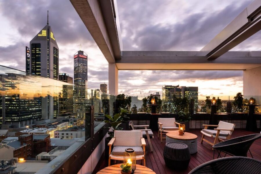 Luxury rooftop bar with city skyline view at dusk, outdoor lounge seating, candles, and heaters.