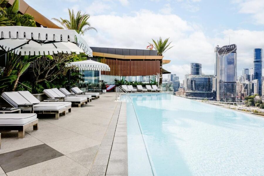 Luxury rooftop infinity pool with sun loungers, umbrellas, and panoramic modern city skyline view.