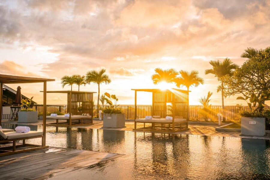 Luxury Bali rooftop infinity pool with wooden cabanas and palm trees at golden sunset.