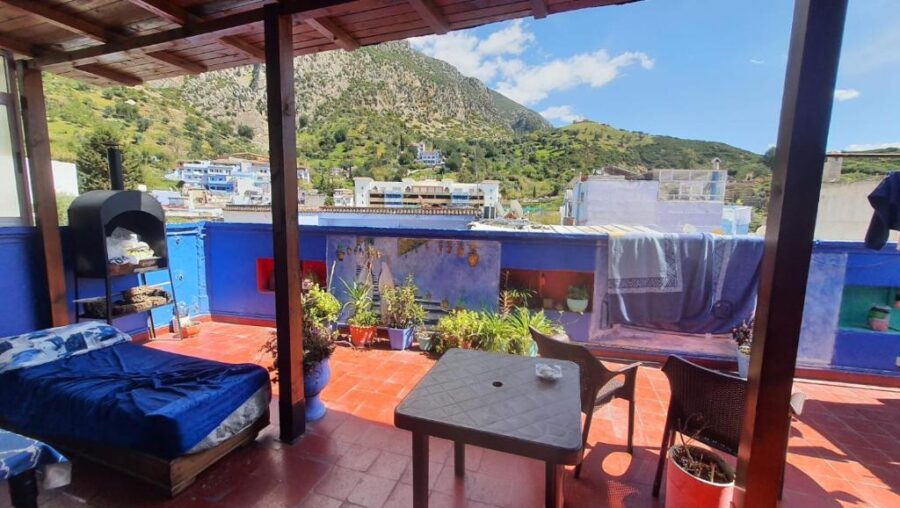 Colorful rooftop terrace in Chefchaouen with blue walls, mountain view, daybed, plants, and seating.