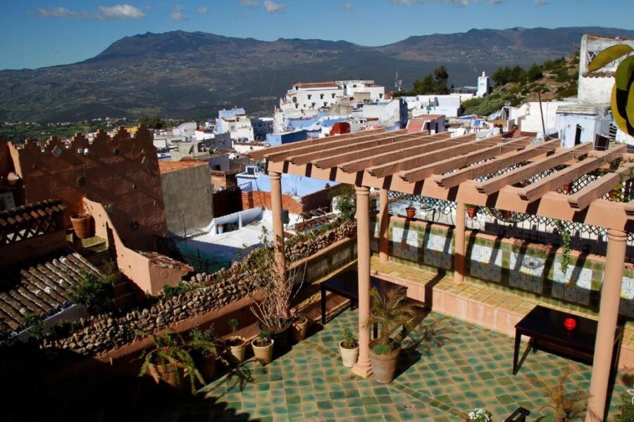 Rooftop terrace in Chefchaouen riad with potted plants overlooking blue town and Rif Mountains.