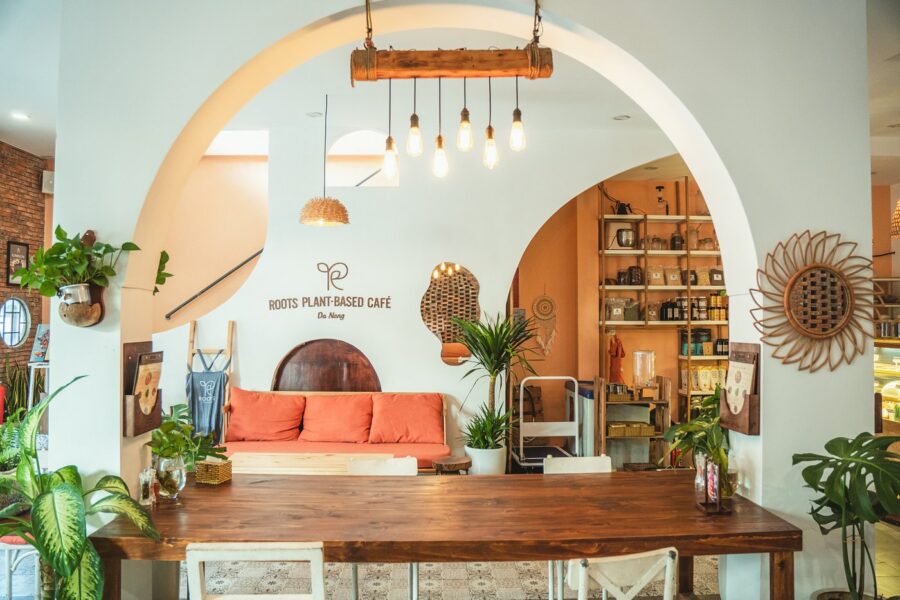 Cozy Roots plant-based café interior in Da Nang with wooden communal table, plants, and warm lighting.