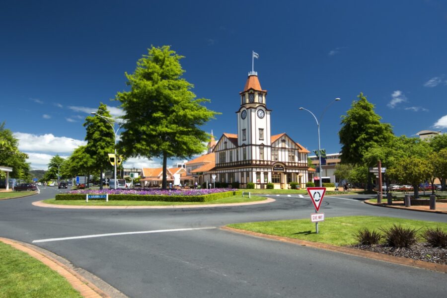 Rotorua Information Centre with Tudor-style clock tower behind roundabout and gardens, New Zealand tourism landmark.