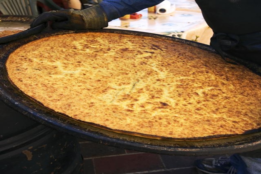 Golden flatbread on metal tray, outdoor market setting, culinary craftsmanship, communal dining.