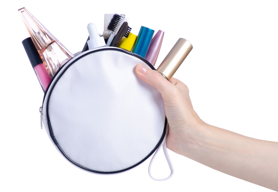Hand grips a white cosmetic bag containing an assortment of makeup items, highlighting its practical use for beauty enthusiasts.