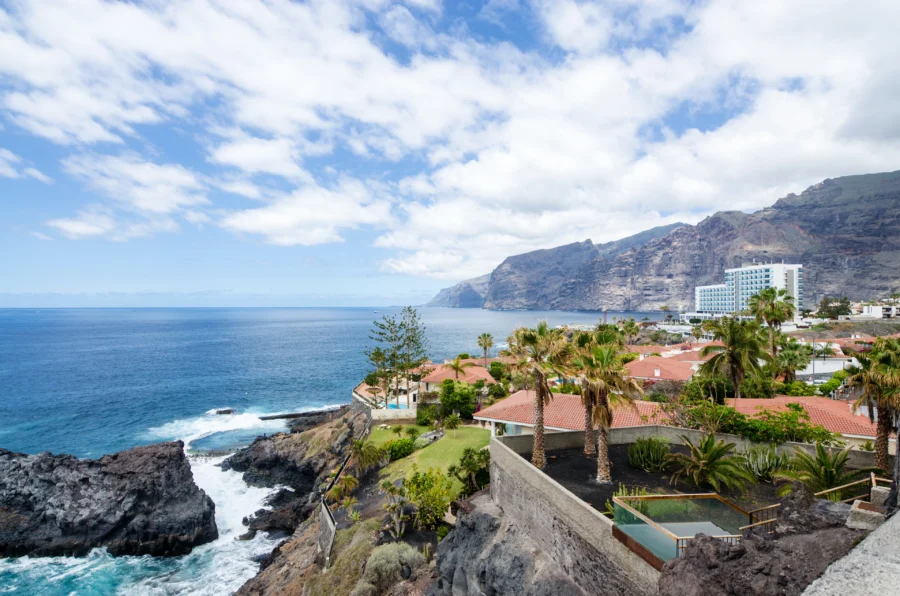 Tenerife cliffside coastline with volcanic rocks, ocean, palm trees, terraces, and sea pools.